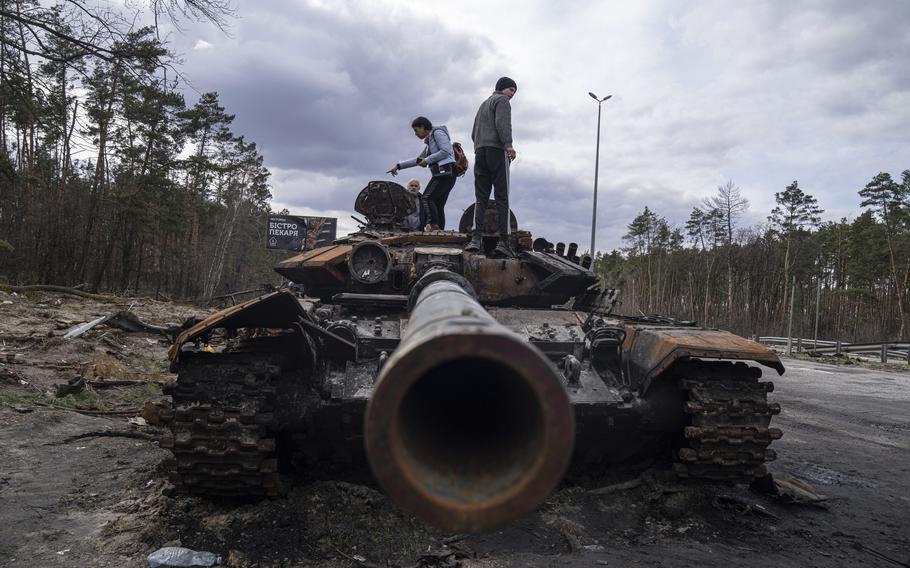 Local residents stand atop of a Russian tank damaged during fighting between Russian and Ukrainian forces in the outskirts of Kyiv, Ukraine, on Monday, April 11, 2022. 