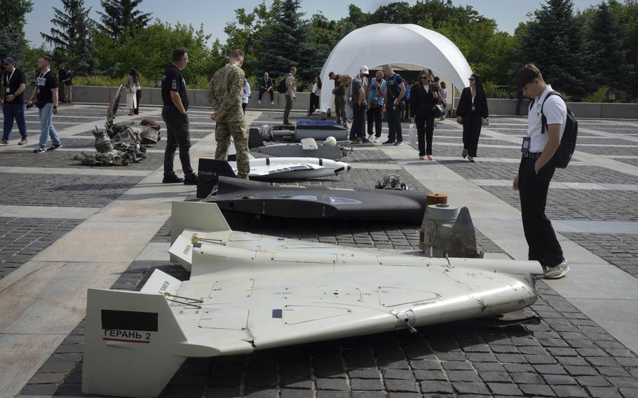 several people look at damaged Russian drones that are lined up on a pavement in Kyiv, Ukraine. 