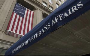 A blue awning, seen from below, reads “Department of Veterans Affairs” outside a government building with a U.S. flag hanging above it.