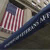 A blue awning, seen from below, reads “Department of Veterans Affairs” outside a government building with a U.S. flag hanging above it.