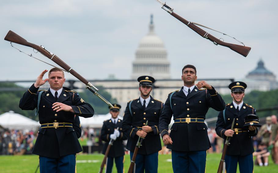 Two soldiers toss rifles in the air as other soldiers watch with the U.S. Capital in the background.