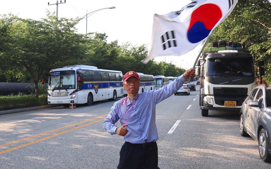 A demonstrator who supports the U.S. military presence in South Korea was the national flag at cars exiting the main gate at Camp Humphreys, South Korea, Thursday, July 27, 2023.
