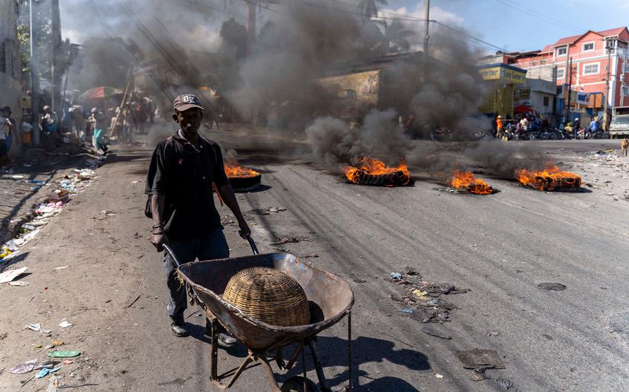 A man pushes a wheelbarrow near burning tires during a day of protest after the deaths of 6 police officers in Port-au-Prince, Haiti, on Jan. 27, 2023. 