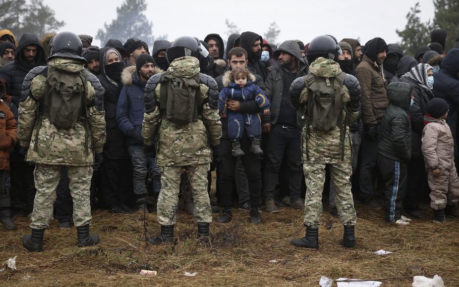 Migrants stand in front of Belarusian troops as they gather in a camp near the Belarusian-Polish border in the Grodno region on November 14, 2021. 