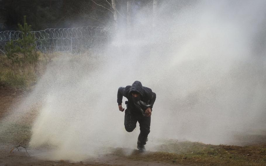 A man runs away from a water cannon during clashes between migrants and Polish border guards at the Belarus-Poland border near Grodno, Belarus, on Tuesday, Nov. 16, 2021. Polish border forces say they were attacked with stones by migrants at the border with Belarus and responded with a water cannon. The Border Guard agency posted video on Twitter showing the water cannon being directed across the border at a group of migrants in a makeshift camp.