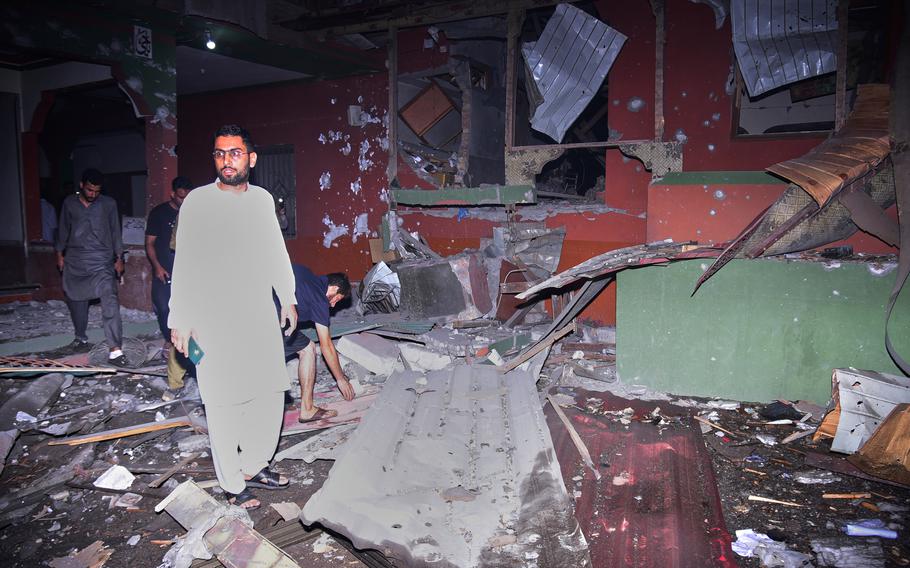 Pakistani residents walk through a destroyed building, with debris strewn about the ground.