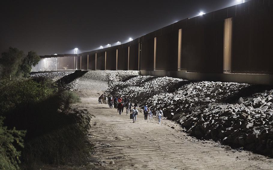 Migrants walks along the border fence before surrendering to U.S. Border Patrol agents, in Yuma, Arizona, on May 10, 2023.