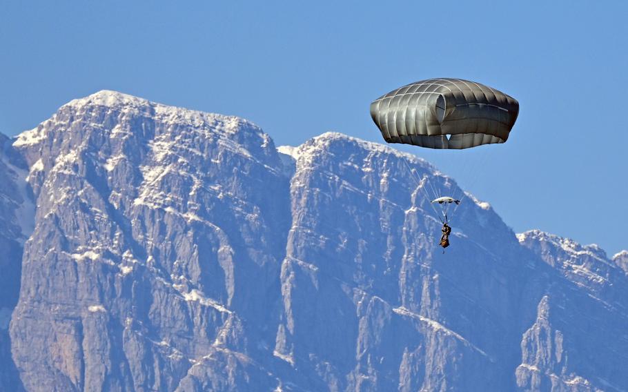 A paratrooper floats to the ground with a parachute after jumping in front of a mountain.