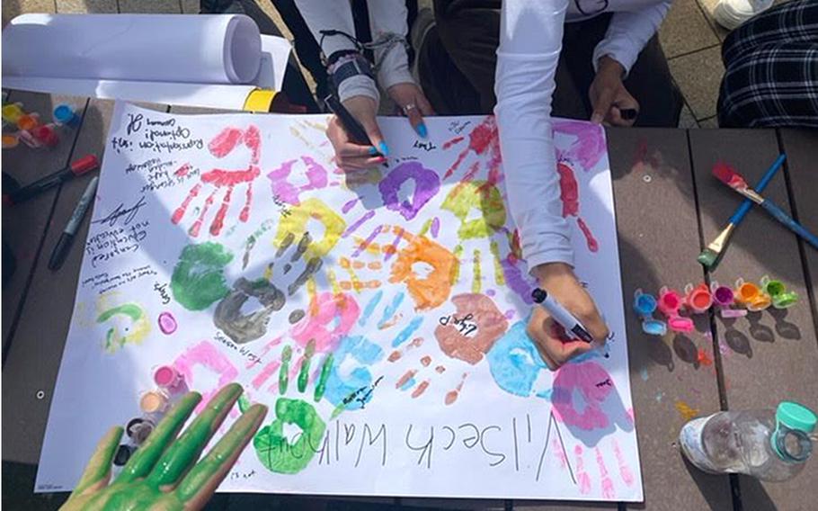 A close-up view of high school students making a banner with colored handprints and messages of protest.