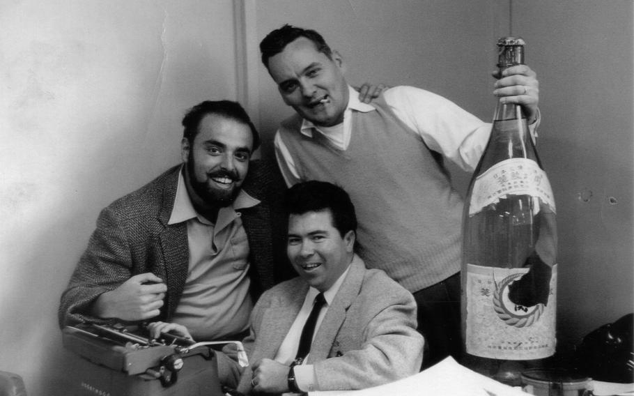 Three men pose for a picture with a giant bottle of Sake