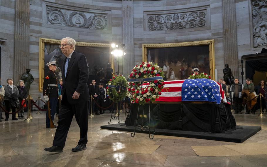 Mitch McConnell walks away from the flag-draped casket of Jimmy Carter.