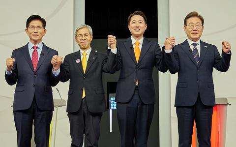 Four South Korean presidential candidates in suits stand next to each other in a line on a stage while holding up their linked hands.