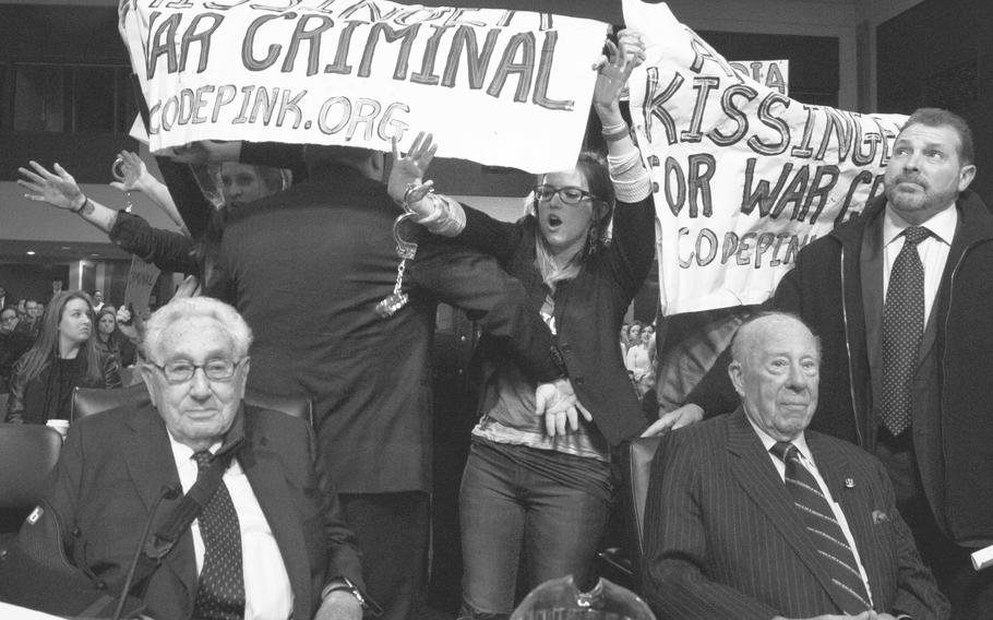Former Secretaries of State Henry Kissinger, left, and George Shults wait for order to be restored during a protest at the start of a hearing of the Senate Armed Forces Committee in Washington, Jan. 29, 2015.
