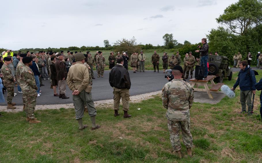 U.S. troops and World War II reenactors listen to a man speak.