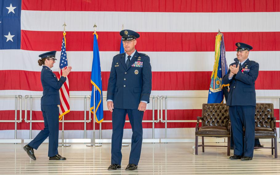 Two Air Force members applaud a third as he walks across a stage.