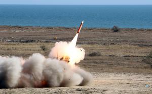 A missile launches from a ground position as fire and smoke emerge from the tail.