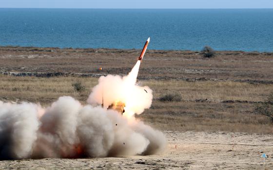 A missile launches from a ground position as fire and smoke emerge from the tail.