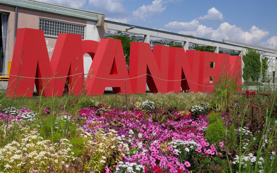 Flowers bloom in front of large letters that spell out “Mannem,” the slang name for Mannheim, Germany. The building behind it was once a U.S. Army warehouse at the former Spinelli Barracks.