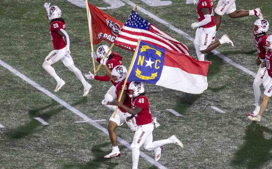 North Carolina State football players run across the football field carrying flags.