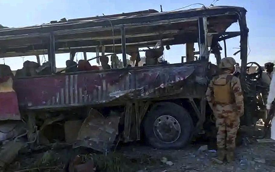 The husk of a damaged bus is surveyed by a service member or security officer.