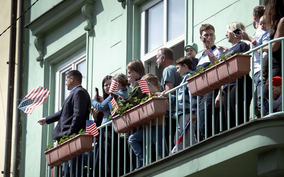 A spectator, among a group on a balcony, waves a small American flag.
