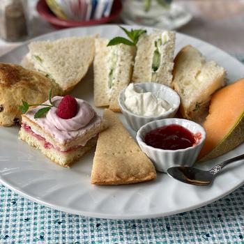 Close-up view of a plate with small sandwiches and pastries sitting on a blue checkered placemat.