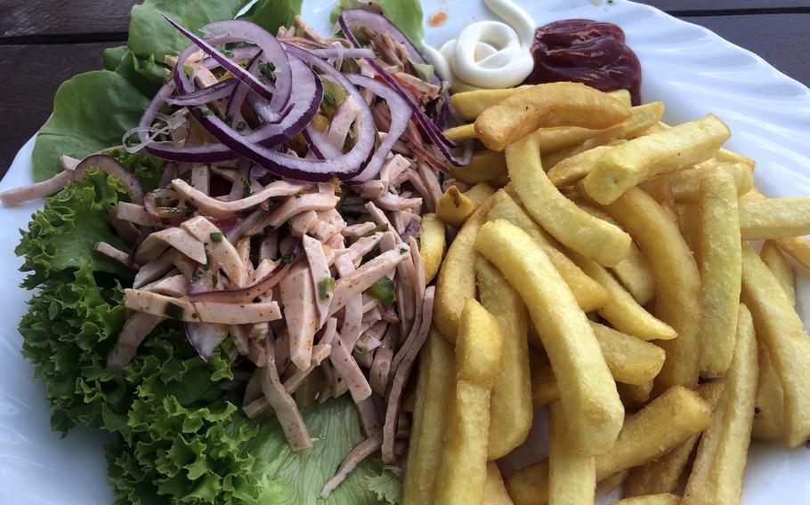 Wurst salad, or sausage salad, served with fries at the Biergarten in Darmstadt, Germany. It’s made with sliced cold cuts and pickles in a vinegar dressing and is topped with red onions. 