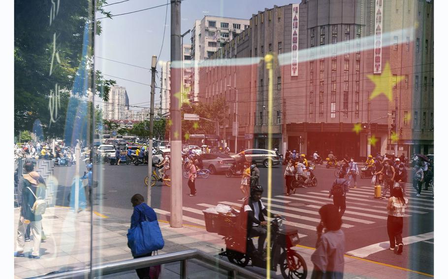 Chinese flags and pedestrians are reflected in a window in Shanghai, China, on June 2, 2023. 
