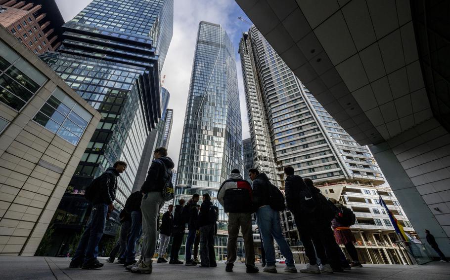 A ground-level shot of people standing before glassy skyscrapers.