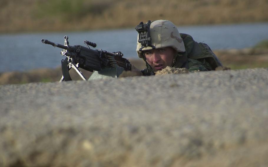 A Marine sqaud automatic machine gunner takes cover behind a drop-off on the edge of a road