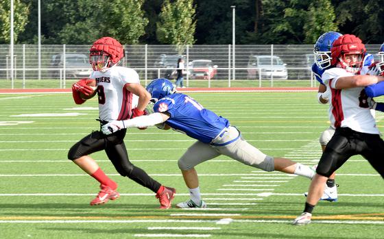 Royal linebacker Landon Torroll, middle, lunges after Kaiserslautern running back Andy Etchell, left, during an Aug. 25, 2023, scirmmage at Ramstein High School on Ramstein Air Base, Germany.