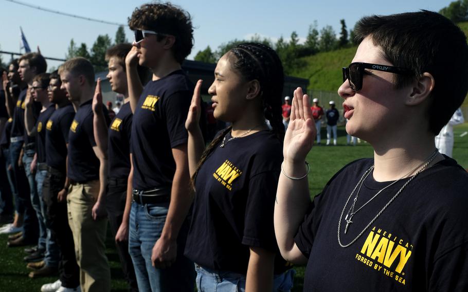 Men and women raise their right hands and take the oath. They are wearing Navy T-shirts.