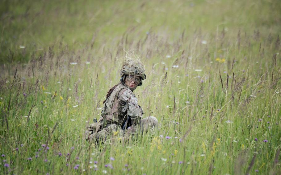A British cadet crouches in tall grass during a live-fire drill. 