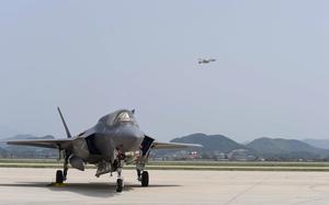 A U.S. Air Force F-35A Lightning II stands ready on the flight line as another jet flies over.