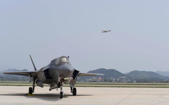 A U.S. Air Force F-35A Lightning II stands ready on the flight line as another jet flies over.