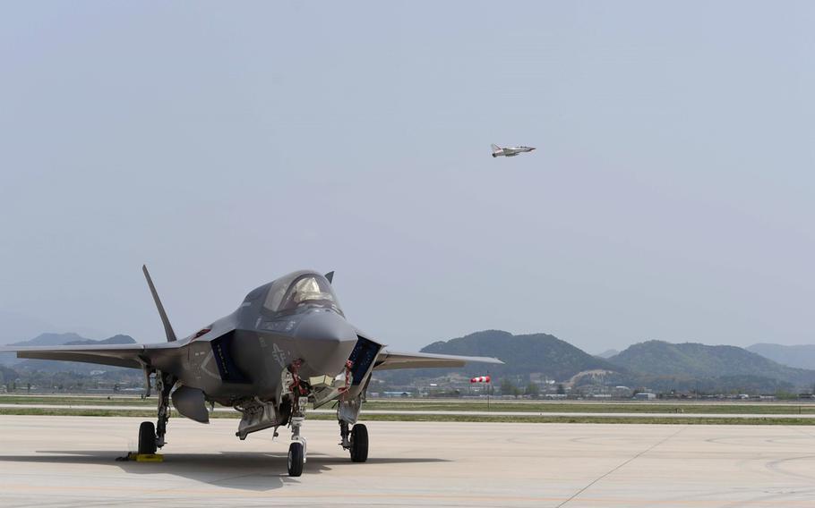 A U.S. Air Force F-35A Lightning II stands ready on the flight line as another jet flies over.