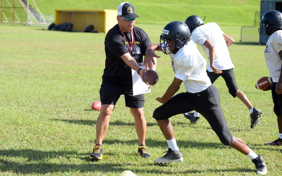 Kadena's Derryck Miller takes a handoff from assistant coach Frank Macias during Monday's practice.