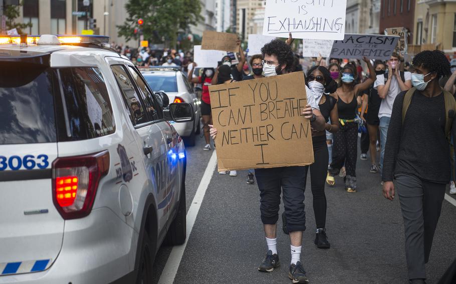 A protester carrying a sign stares inside a police vehicle as he and thousands of other demonstrators marched through the streets of Washington, D.C. within blocks of the White House on Friday, May 30, 2020. The march participants were protesting the death of George Floyd.