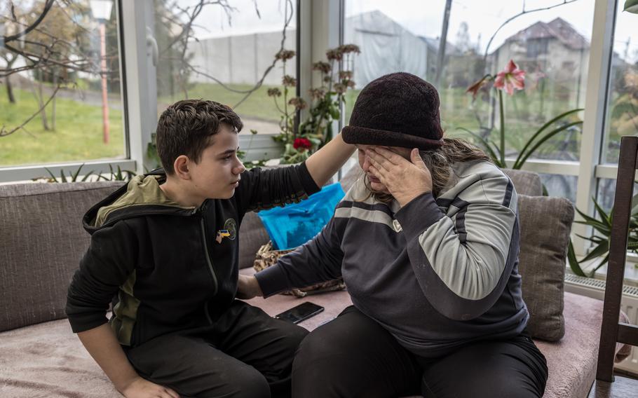 A boy pats his grandmother’s head as she wipes tears from her face.