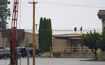 Two FBI investigators on July 14, 2024, in Butler, Pa., scan the roof of AGR International Inc, the building adjacent to the Butler Fairgrounds, from which Matthew Thomas Crooks fired, in an attempted assassination, at former President Donald Trump during a campaign rally on July 13.