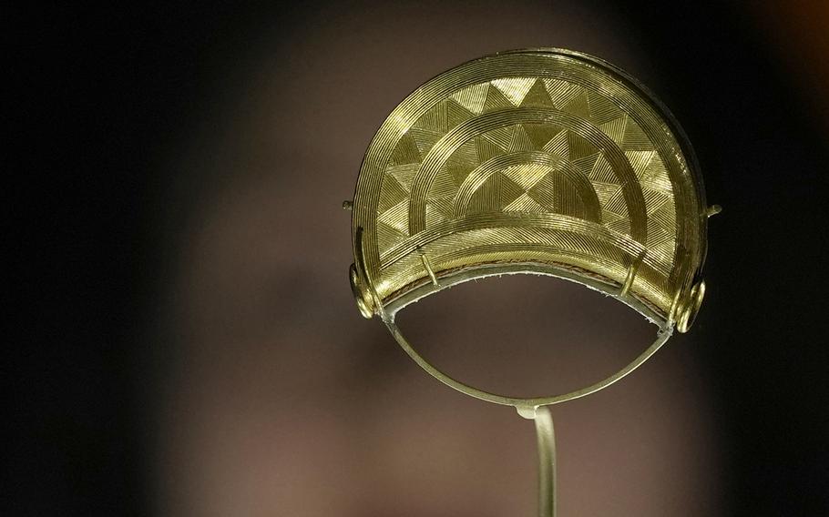 A member of staff poses next to a gold brooch from Shropshire, England. 1000 BCE, on display at the The World of Stonehenge’ exhibition at the British Museum in London, Monday, Feb. 14, 2022. The exhibition which displays objects and artifacts from the era of Stonehenge opens on Feb. 17 and runs until  July 17, 2022. 