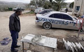 A Palestinian man stands by a car he said Jewish settlers had vandalized slashing its tires and spray painting it with the Jewish Star of David and Hebrew that reads, "Stop administrative detentions," in the village of Qira near the West Bank town of Salfit, Sunday, Jan 23, 2022. (AP Photo/Majdi Mohammed)