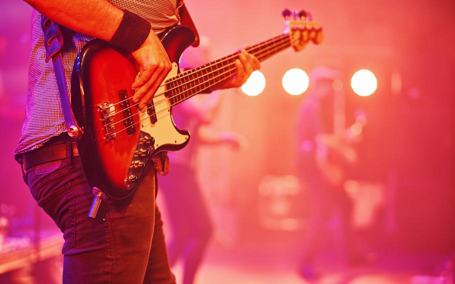 A guitar player’s hands and torso can be seen playing somewhere with moody lighting.