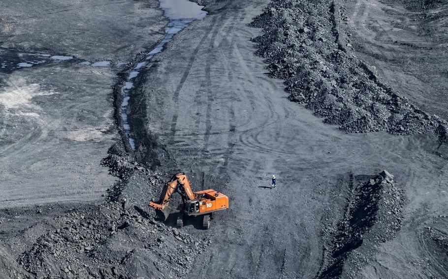 An orange mining vehicle, seen from above, sifts through a pile of rocks with a small figure visible near it.
