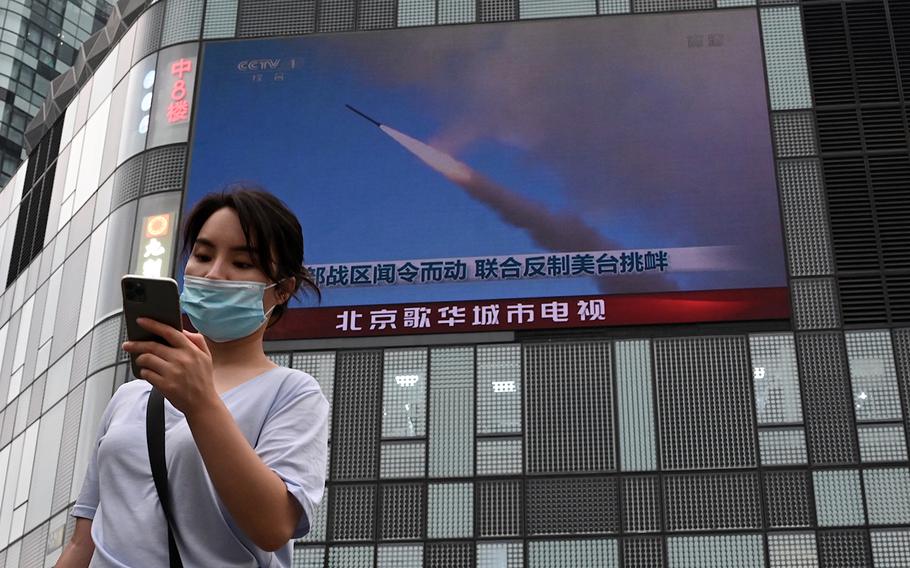 A woman uses her mobile phone as she walks in front of a large screen showing a news broadcast about China’s military exercises encircling Taiwan, in Beijing on Aug. 4, 2022. 