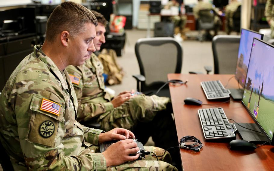 Soldiers seated at a desk with computers in front of them.