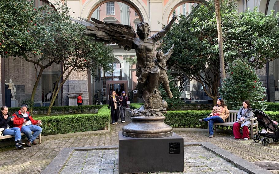 A sculpture of Icarus and Daedalus in a courtyard where people are sitting on benches