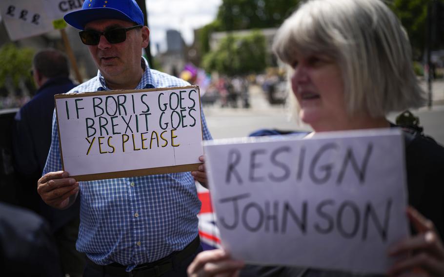 People holds placards as they protest outside the Houses of Parliament, in London, Wednesday, July 6, 2022. 