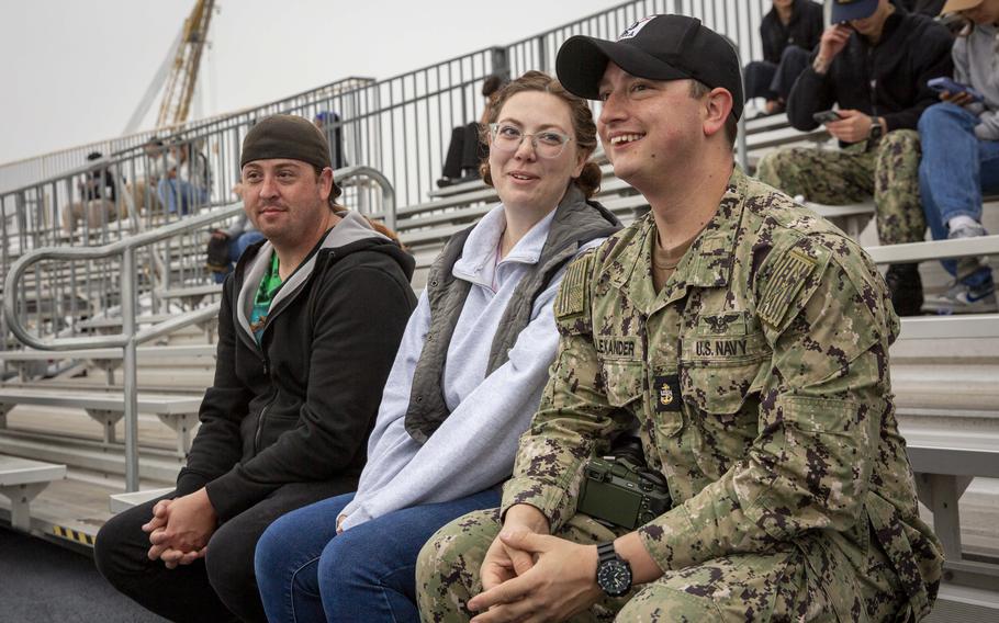 Three people sit together on bleachers 