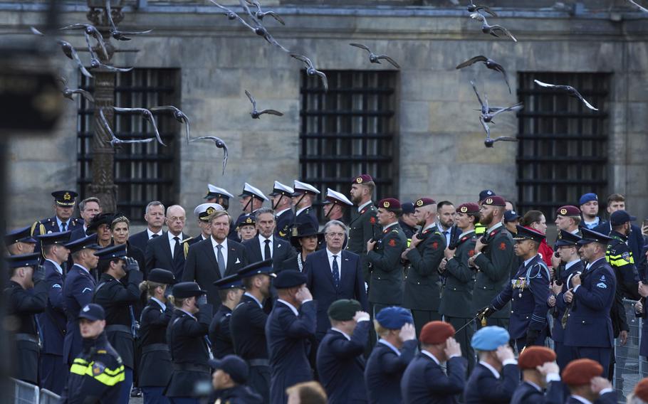 A group of service members in uniform on either side of a group of dignitaries.